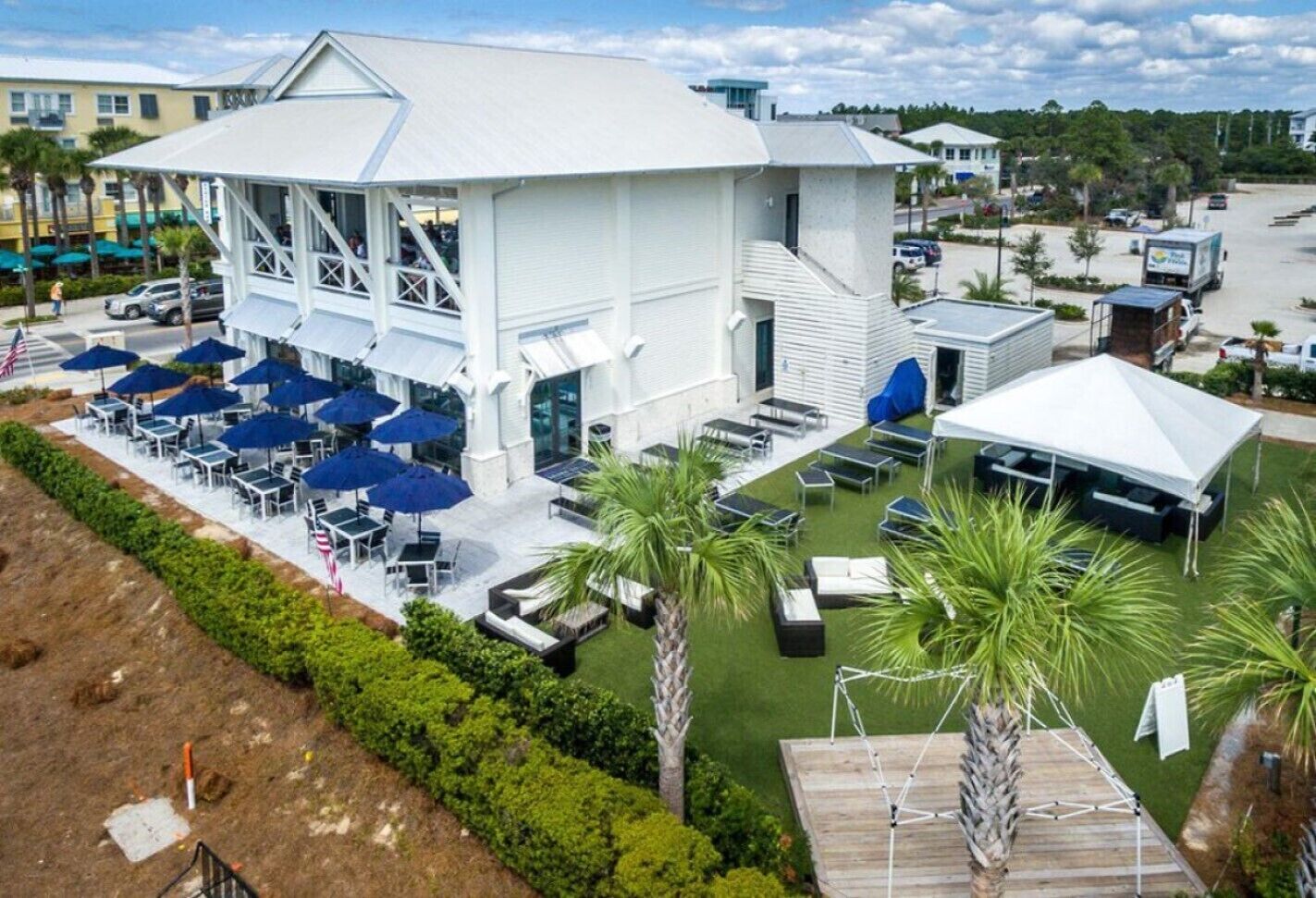 A white building with a covered patio area, outdoor seating, and palm trees.