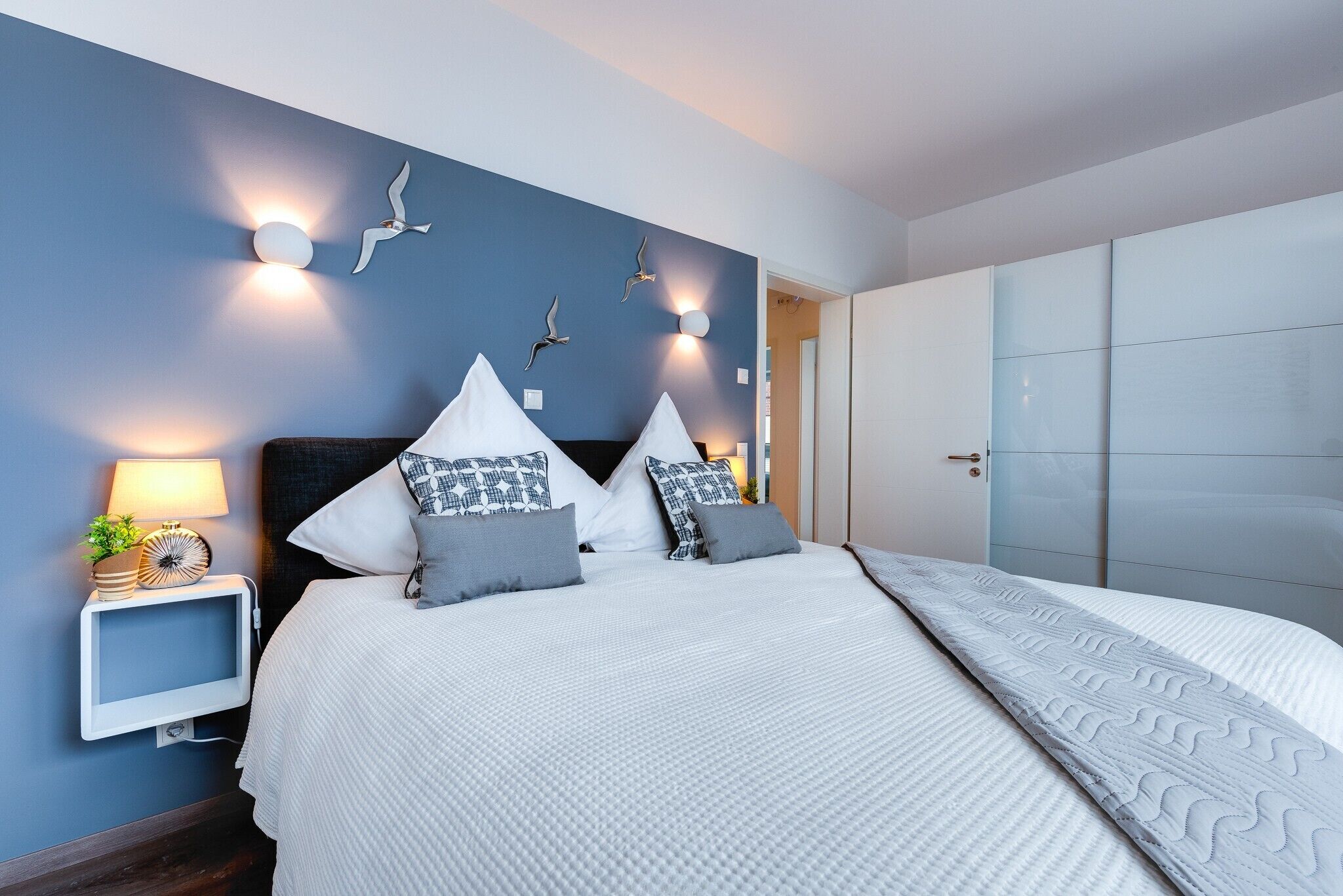 A bedroom with a bed, bedside tables, wall-mounted lights, and a wardrobe.