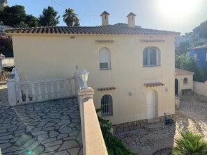 Un bâtiment à deux étages, doté d’un toit recouvert de tuiles, d’un balcon avec une balustrade et d’une cour pavée de pierres.