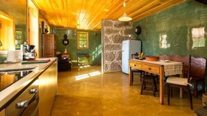 A kitchen with wooden cabinets, a refrigerator, a dining table with chairs, and a stone wall.