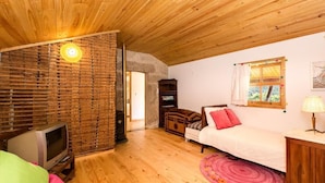 A cozy room with a wooden ceiling, a brick wall, a bed, a TV, and a window with curtains.
