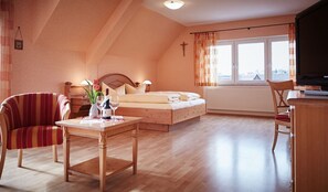 A cozy bedroom with a bed, a wooden table with a vase and a glass, a TV, and a window with curtains. - Metzgereigasthof Rebstock (Ettenheim)