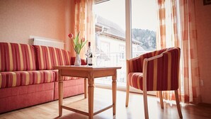 A room with a striped sofa, a wooden table with a vase and wine glasses, and a chair. - Metzgereigasthof Rebstock (Ettenheim)