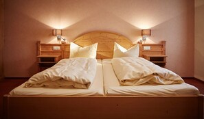 Cama doble con cabecera de madera y mesitas de noche, cada una con una lámpara.