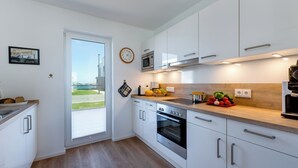 A modern kitchen with white cabinets, stainless steel appliances, and a large window. - Vacation home "Nis Randers" with floor-to-ceiling windows, sauna & view of the Schlei (Olpenitz)