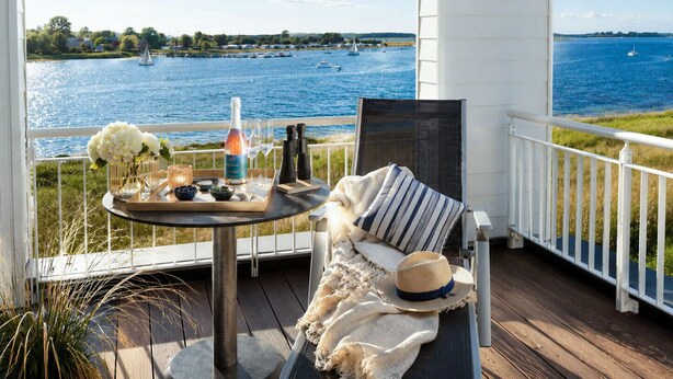 A balcony with a table set for two, overlooking a body of water with boats. - Vacation home "Nis Randers" with floor-to-ceiling windows, sauna & view of the Schlei (Olpenitz)