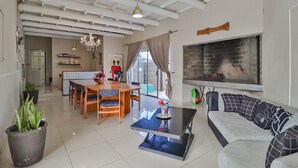 A spacious living area with a dining table, sofa, and a fireplace. - Mauya Guesthouse (Cape Town)