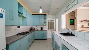 A kitchen with teal cabinets, a white tiled backsplash, a gas stove, and a sink. - Mauya Guesthouse (Cape Town)