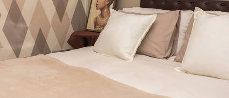 A bed with white and beige pillows, a brown headboard, and a painting on the wall.