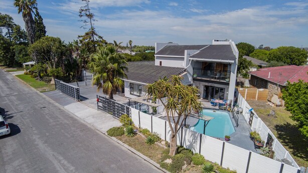 A modern two-story house with a swimming pool, surrounded by a white fence and palm trees. - Mauya Guesthouse (Cape Town)