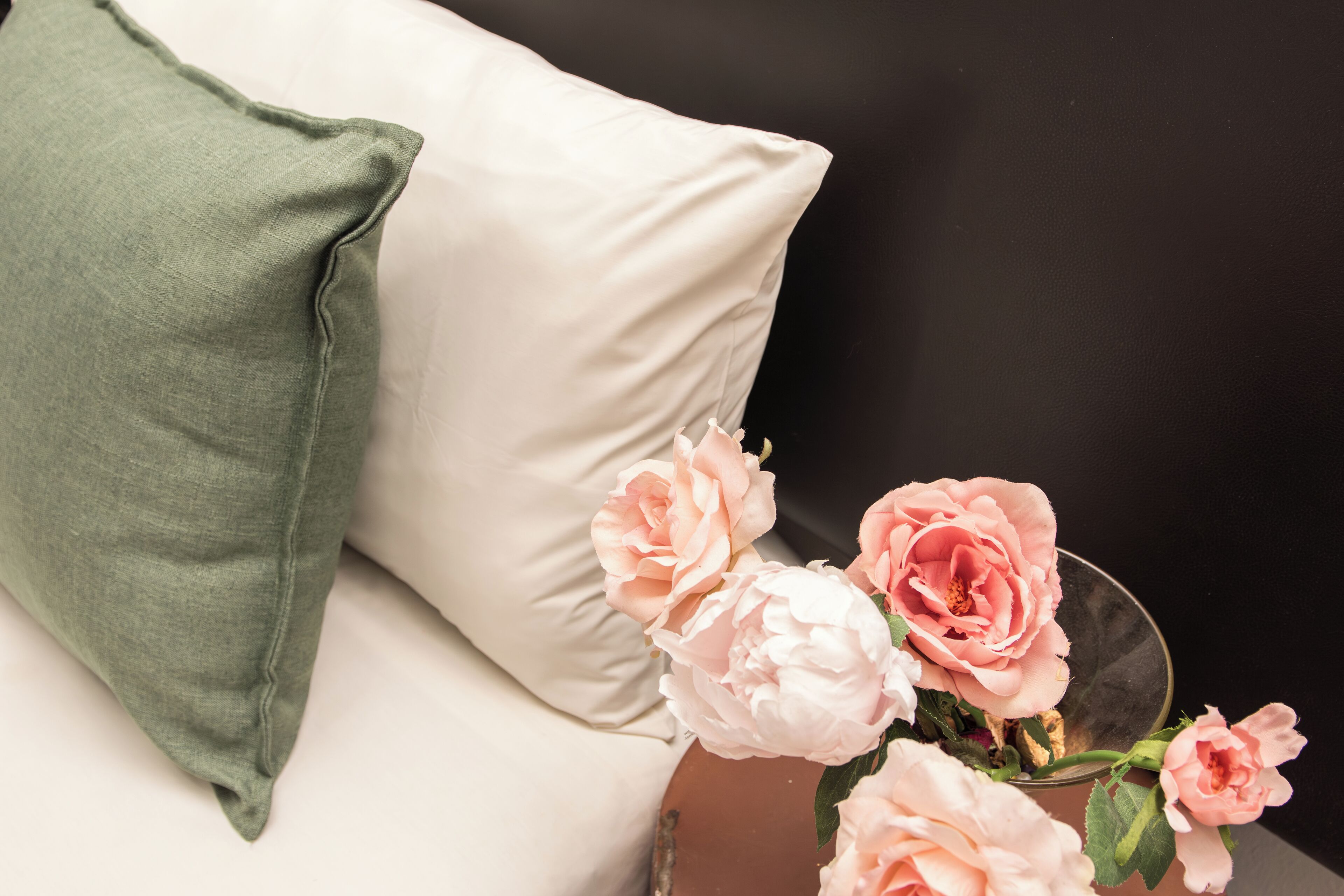 A bed with a white pillow and a green pillow, and a vase with pink flowers.