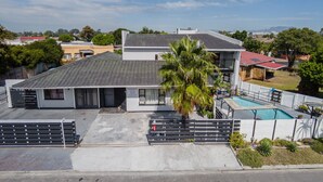 A two-story building with a swimming pool, a covered patio, and a fenced parking area. - Mauya Guesthouse (Cape Town)