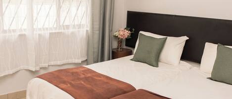 A neatly made bed with white and brown bedding, a dark headboard, and a vase with flowers on a bedside table.