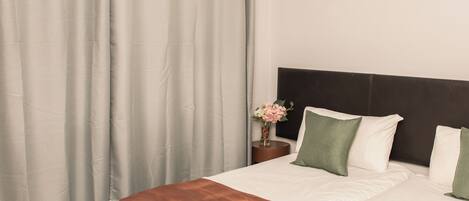 A hotel room with a large bed, a nightstand with a vase of flowers, and a headboard with pillows.