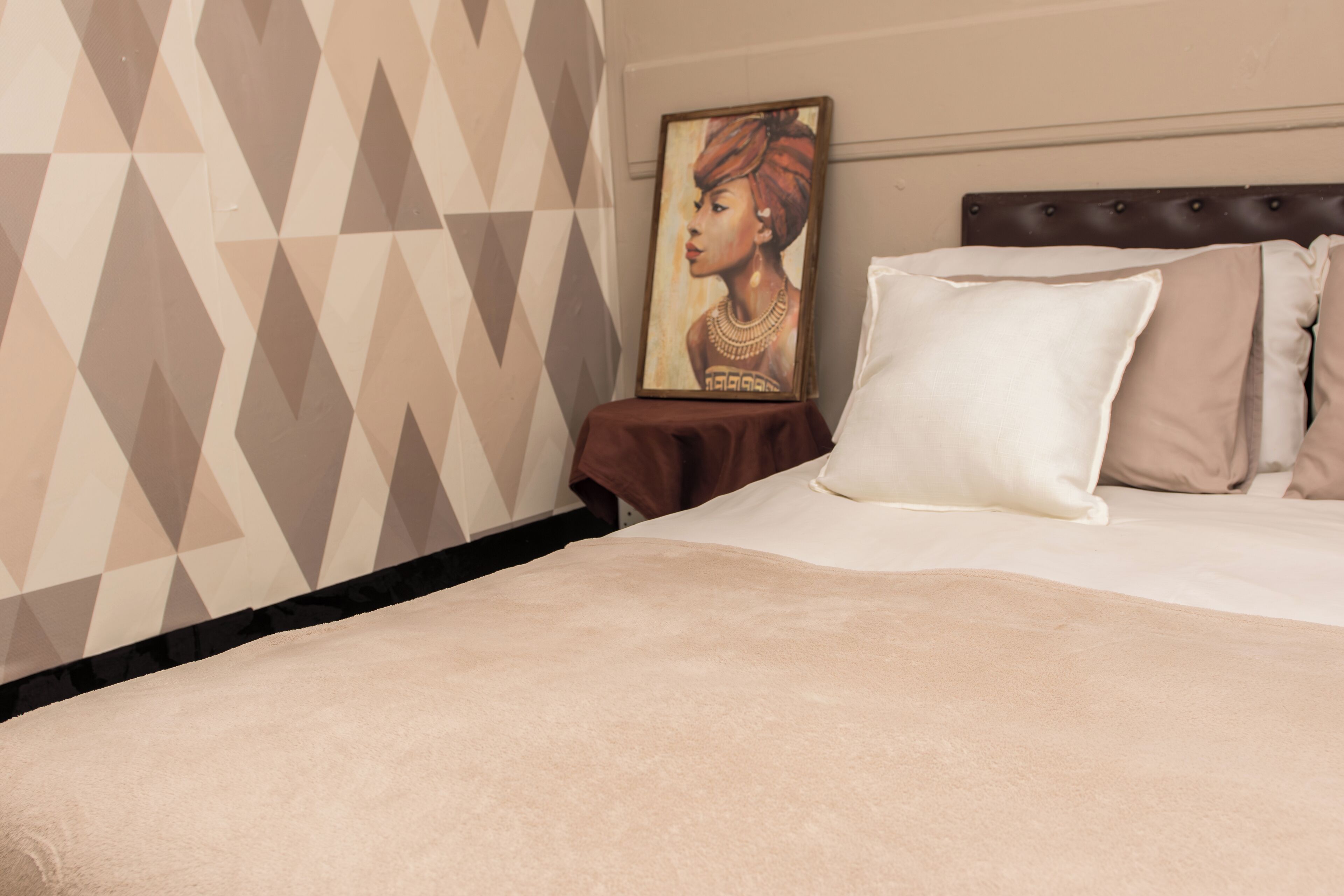 Cama bem arrumada com travesseiro branco e cabeceira marrom. Um quadro emoldurado está pendurado na parede ao lado da cama.