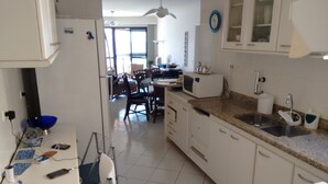 A kitchen with white cabinets, a microwave, a sink, and a dining area with chairs and a table. - Beautiful fit, standing on the sand with spectacular sea views. Spotless (Bertioga)