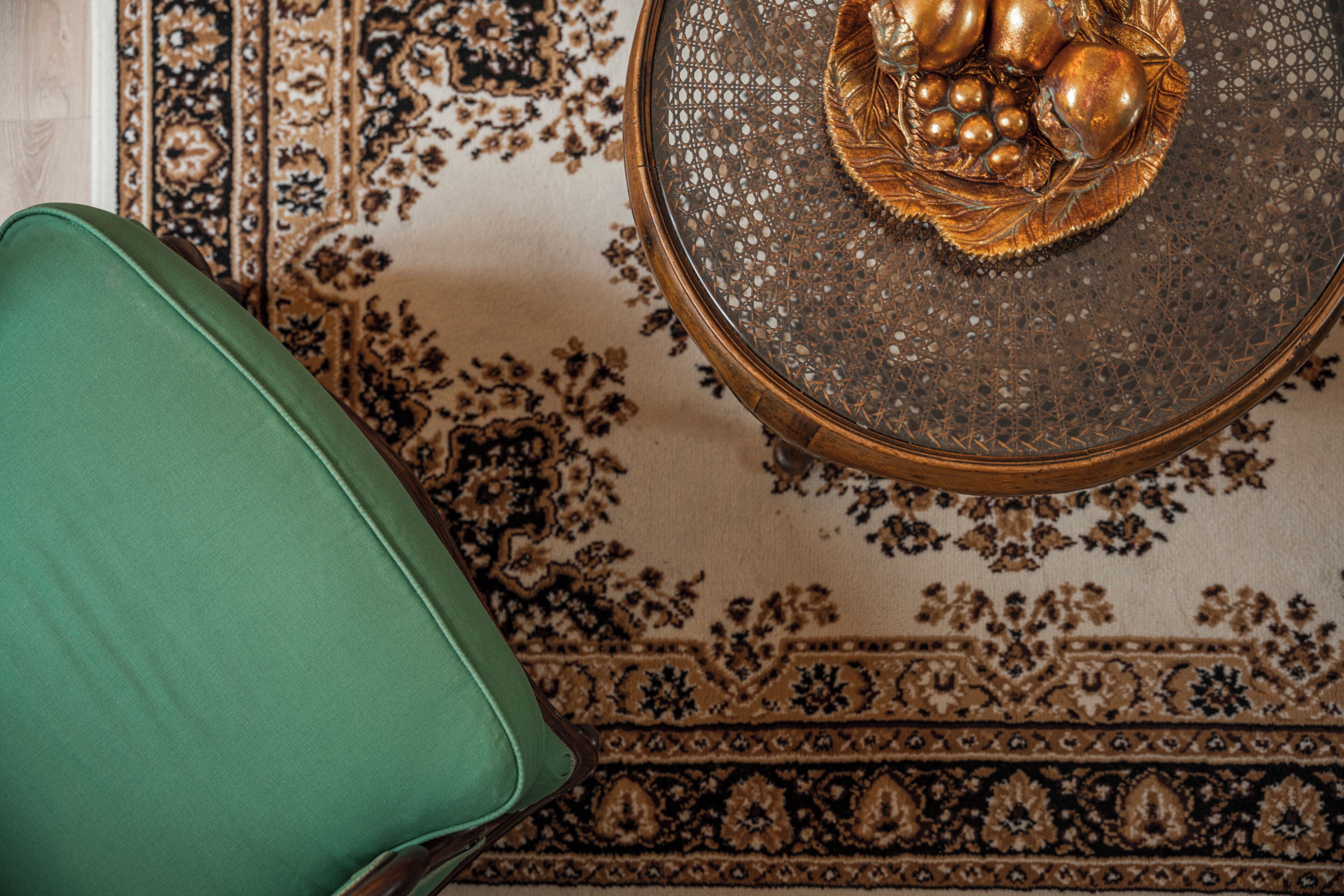 Une chaise verte, une moquette à motifs et une table décorative agrémentée d’un centre de table doré.