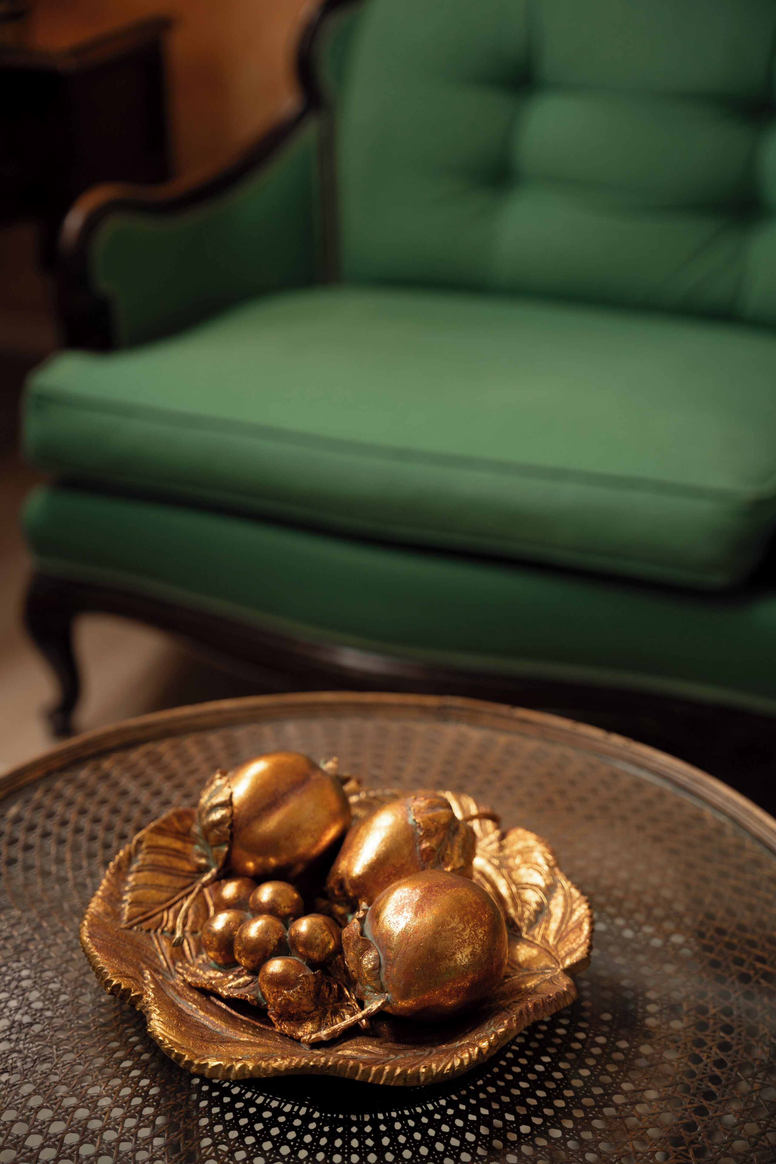 A green upholstered chair, a round table with a decorative tray, and a patterned tablecloth.