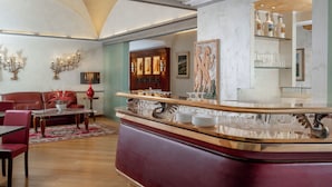 A spacious living room with a red sofa, a coffee table, and a dining area with chairs. - Hotel Roma (Bologna)