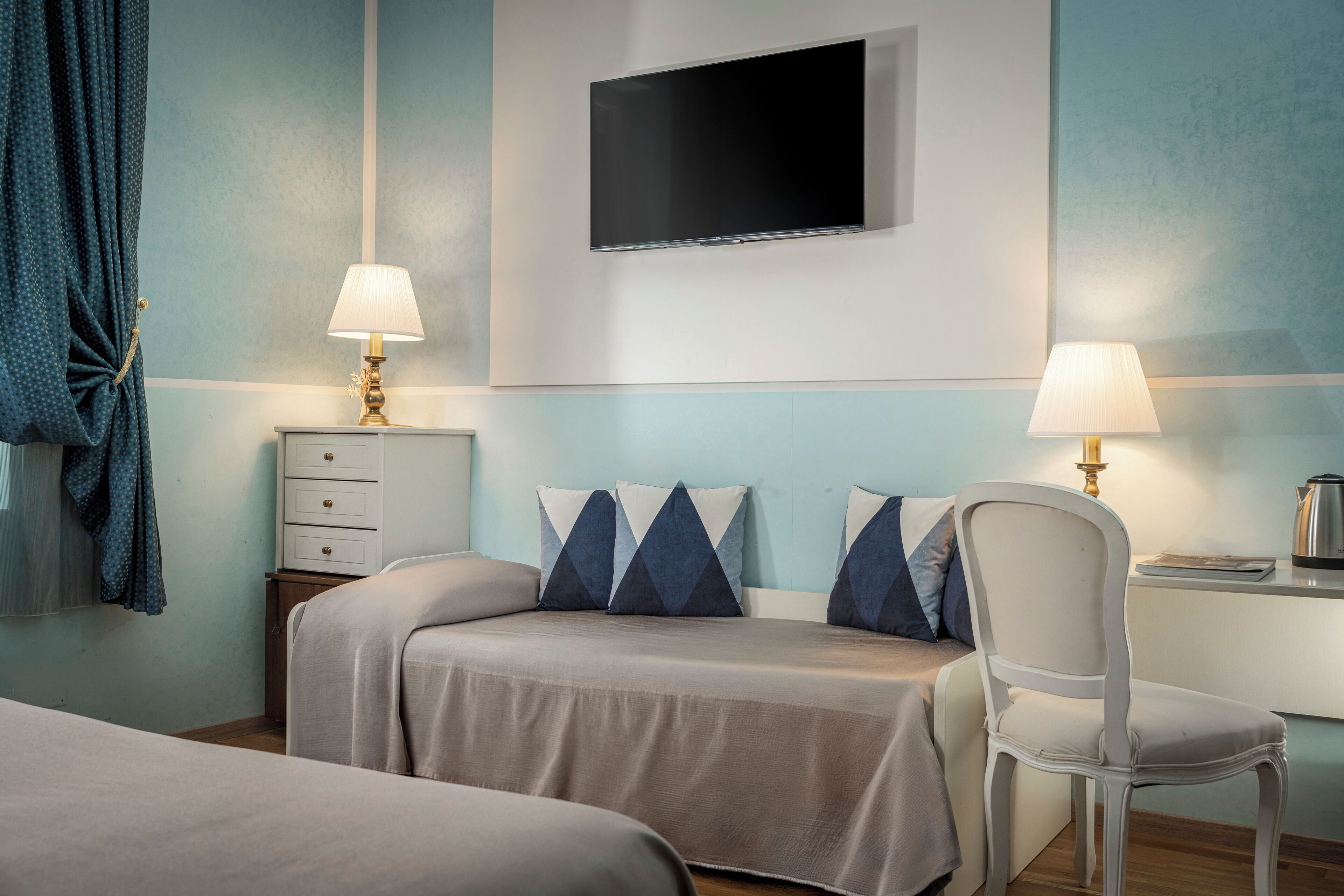 Une chambre d’hôtel comprenant un lit, une chaise, un bureau, un téléviseur et deux lampes.