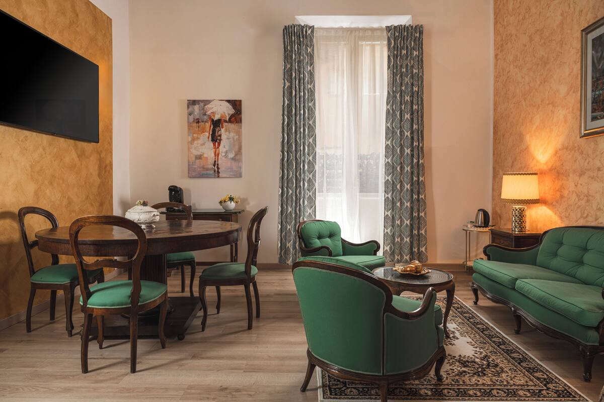 Una sala de estar con una mesa redonda de comedor, sillas tapizadas de verde, un sofá verde y una alfombra estampada.