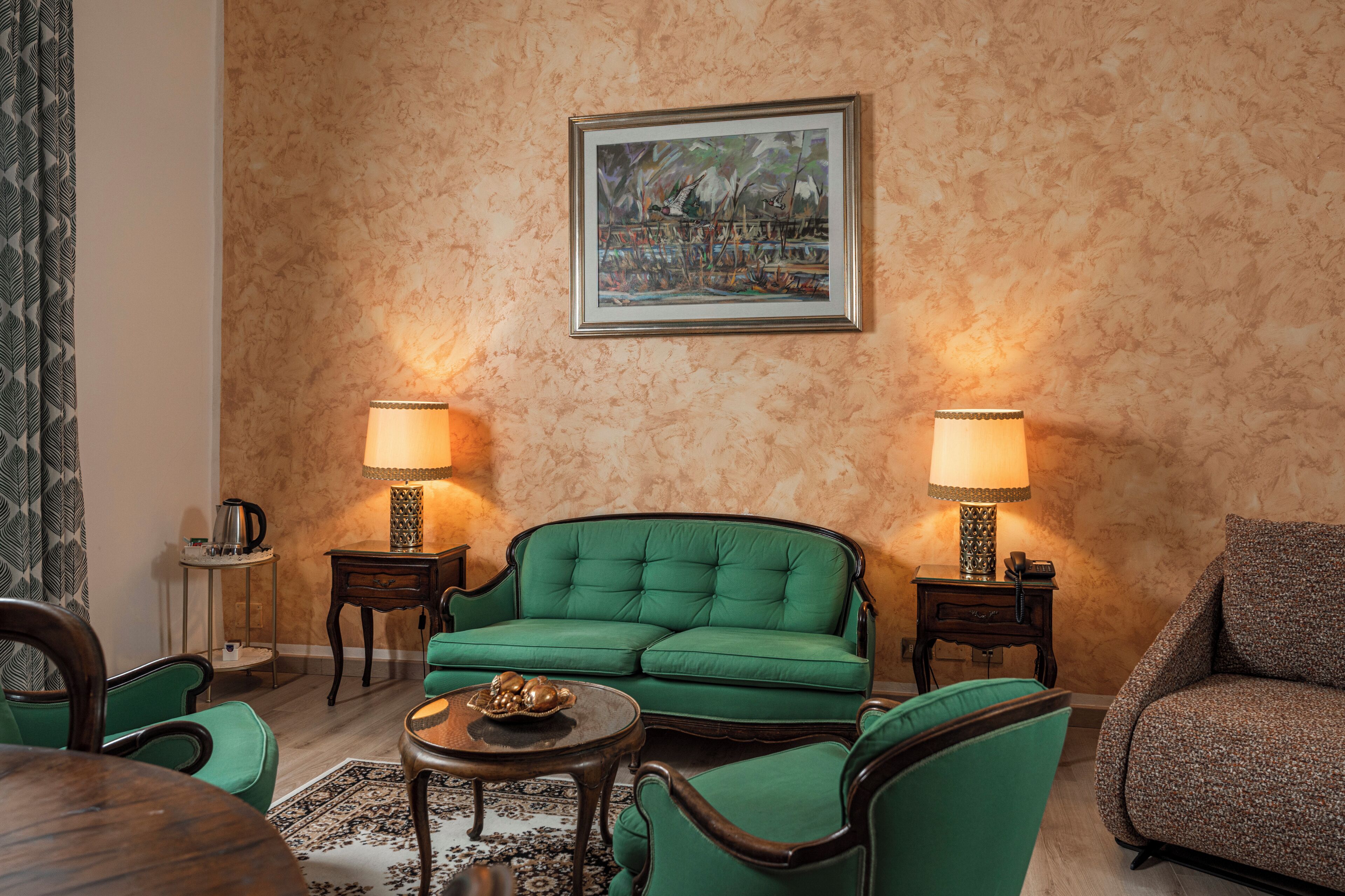 A living room with a green sofa, two side tables with lamps, a coffee table, and a framed painting on the wall.