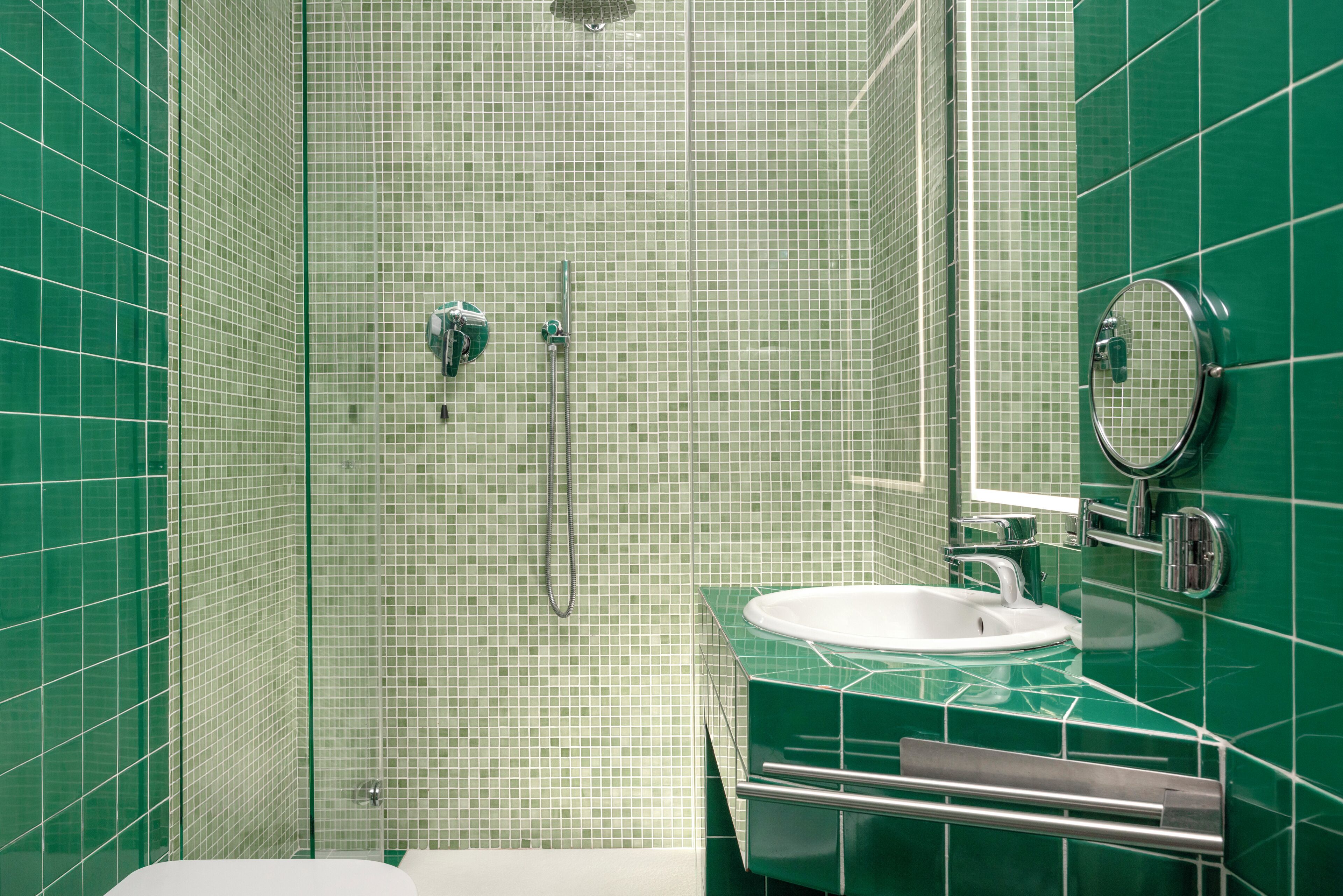 A bathroom with green tiled walls, a white sink, a mirror, and a shower area.