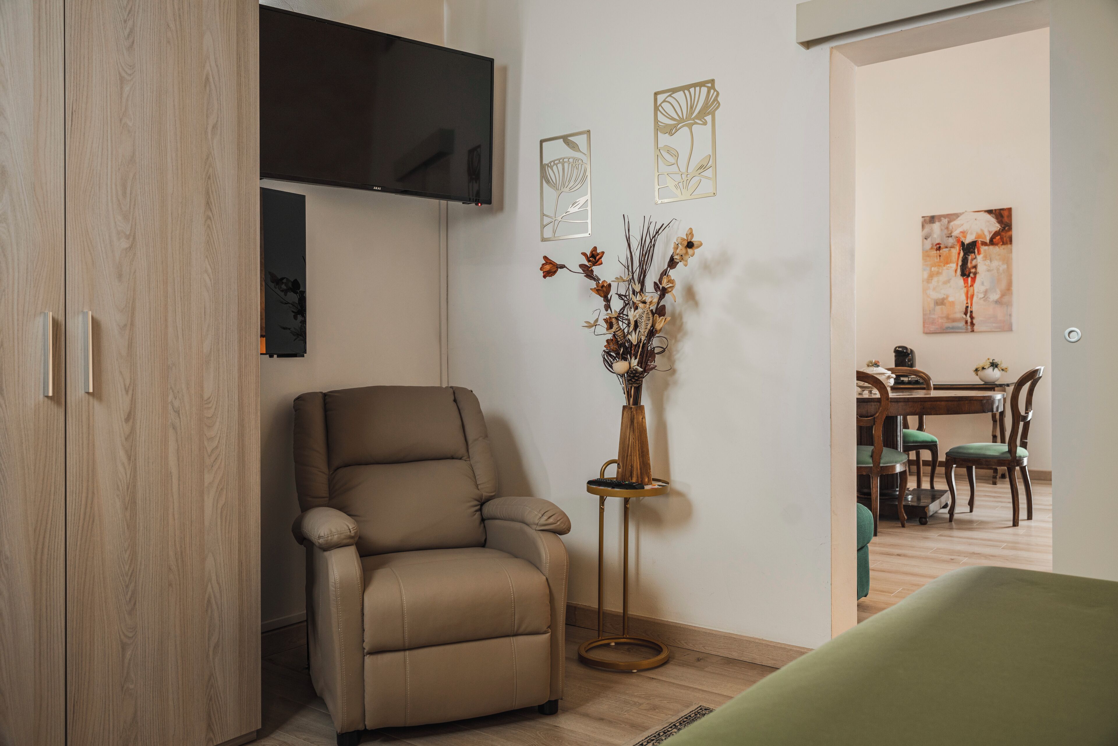Una sala de estar moderna con un sofá de cuero, un televisor de pantalla plana, decoración en la pared, un jarrón con flores secas y un comedor con muebles de madera.