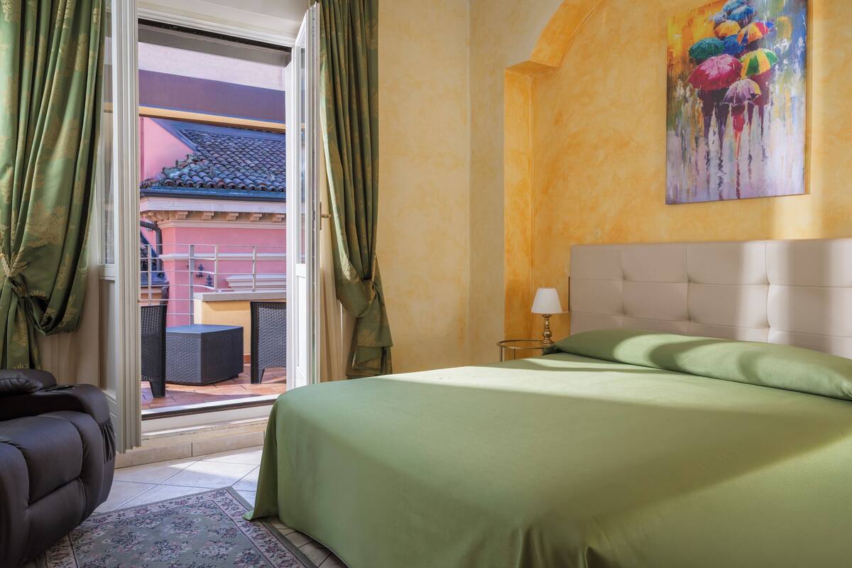 Una habitación de hotel con cama, una silla, una mesa y vistas a un edificio con tejado de tejas.