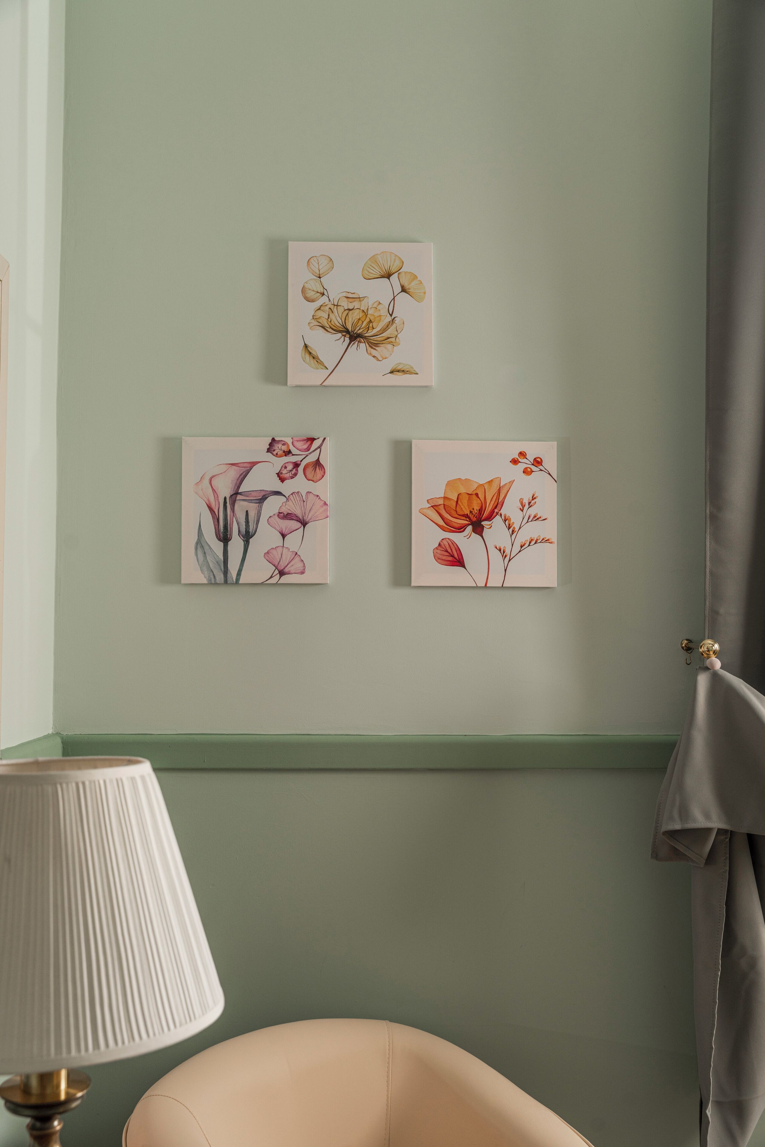 Ein Zimmer mit grüner Wand, einem beigen Sessel und drei floralen Bildern.