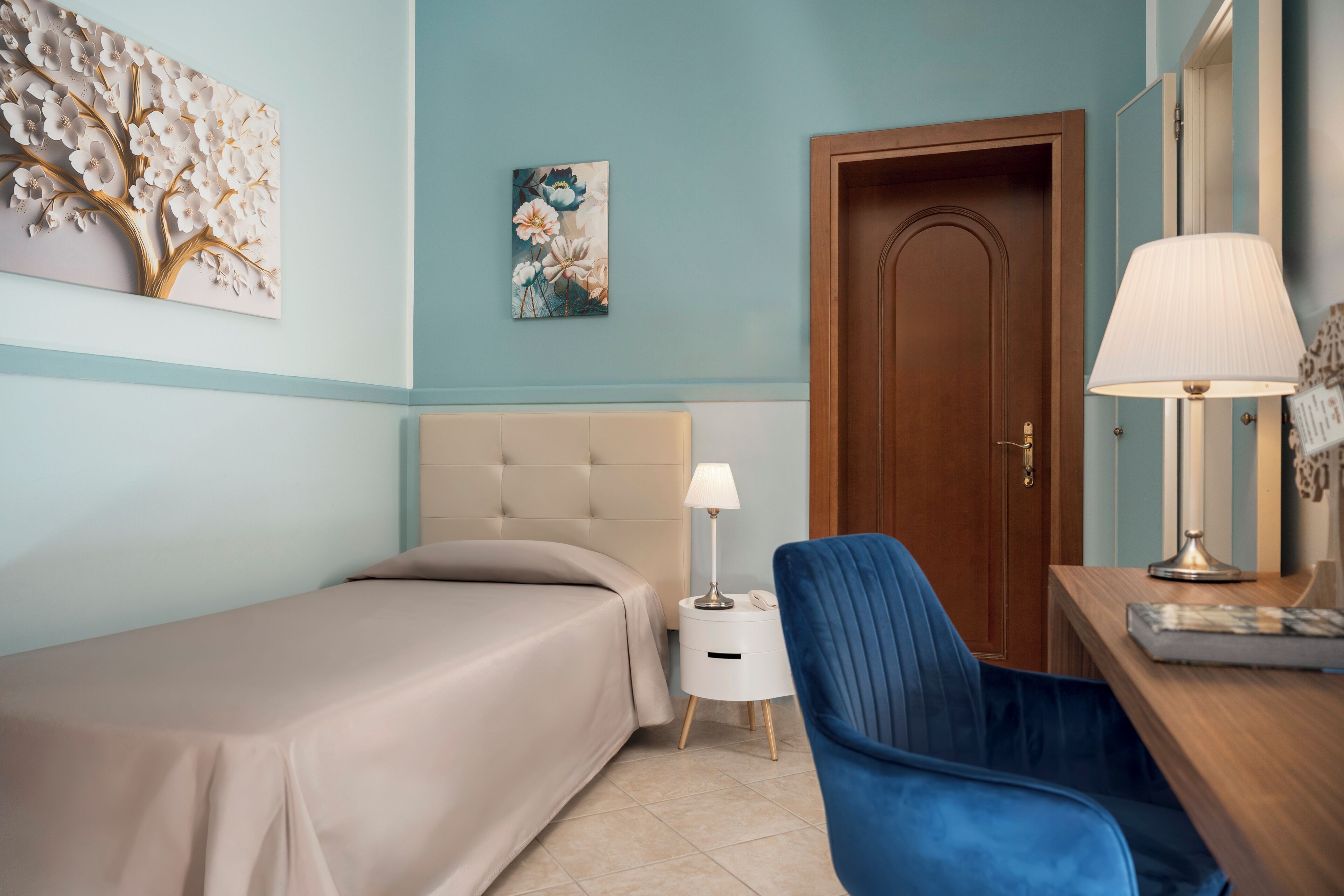 A bedroom with a bed, a desk, a chair, a lamp, and a door.
