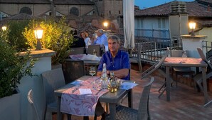 A terrace with tables and chairs, a tower in the background, and a clear sky. - Hotel Roma (Bologna)