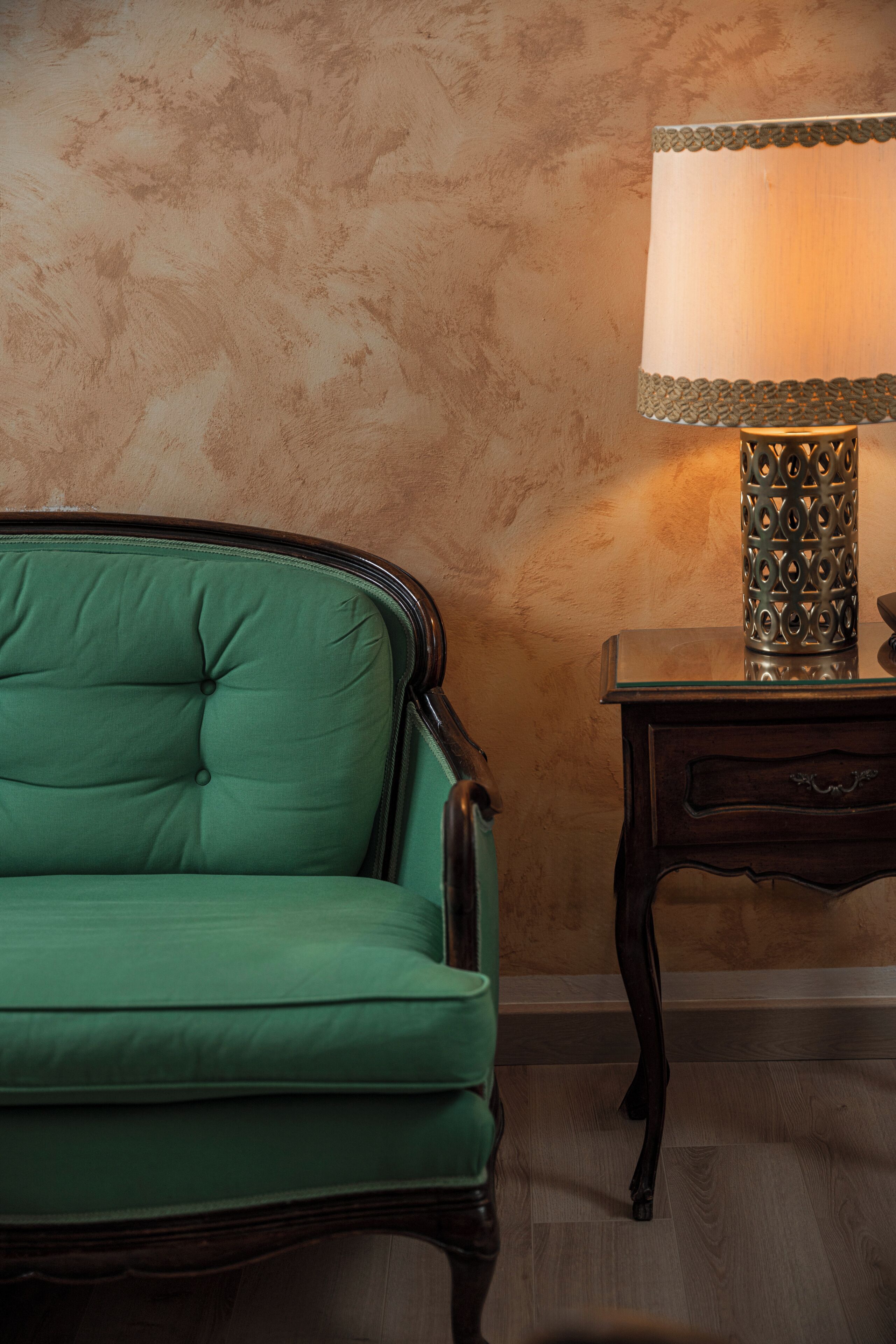 A green upholstered chair, a wooden side table with a lamp, and a textured wall.