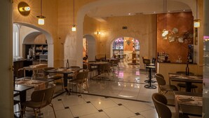 A spacious restaurant with high ceilings, arched doorways, and a central bar area. Tables and chairs are arranged for dining. - Hotel Roma (Bologna)