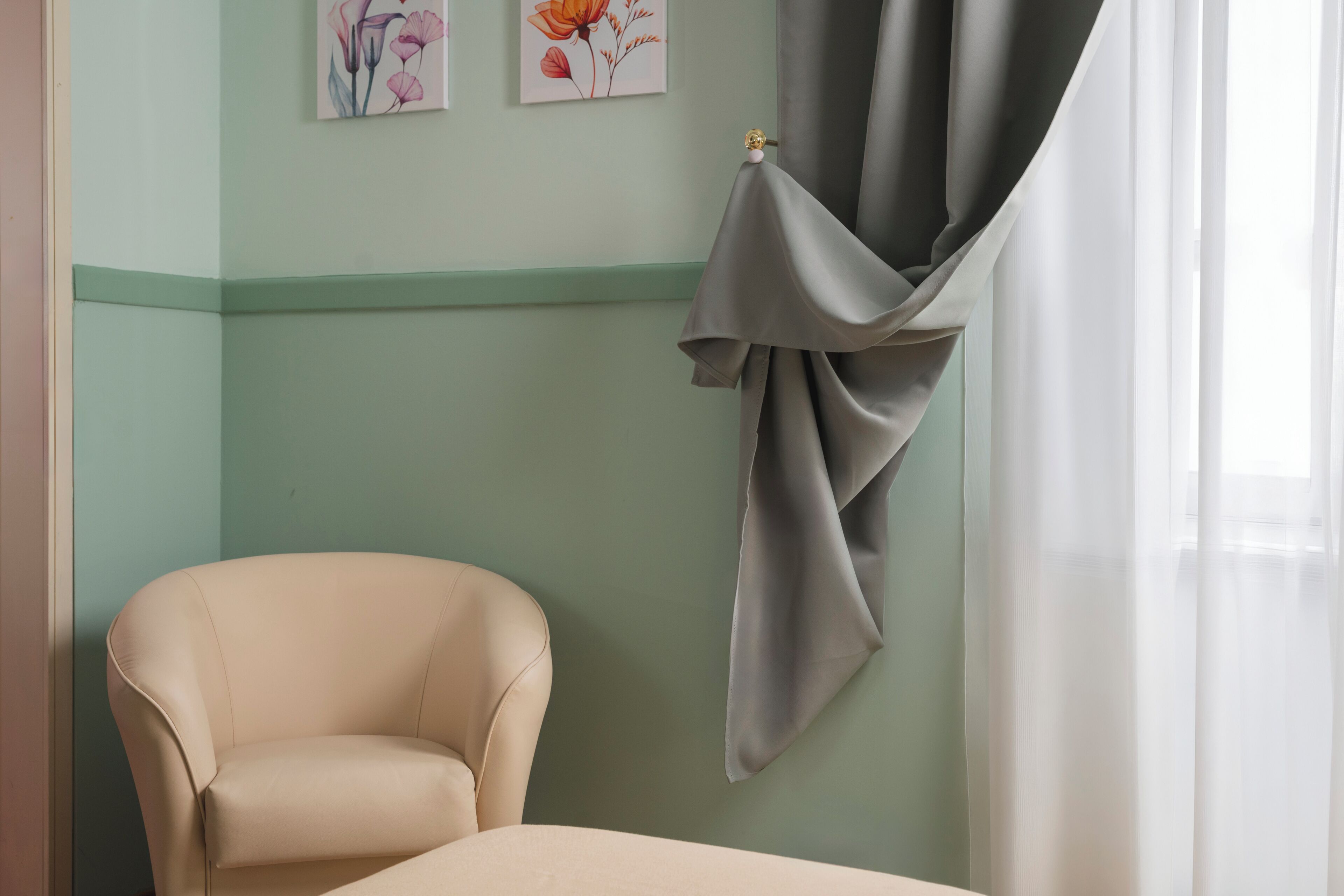 A room with a single beige armchair, a green wall, and a window with a curtain.