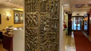 A lobby with a decorative wall featuring intricate carvings, a reception desk, and a red carpet leading to the entrance. - Hotel Roma (Bologna)