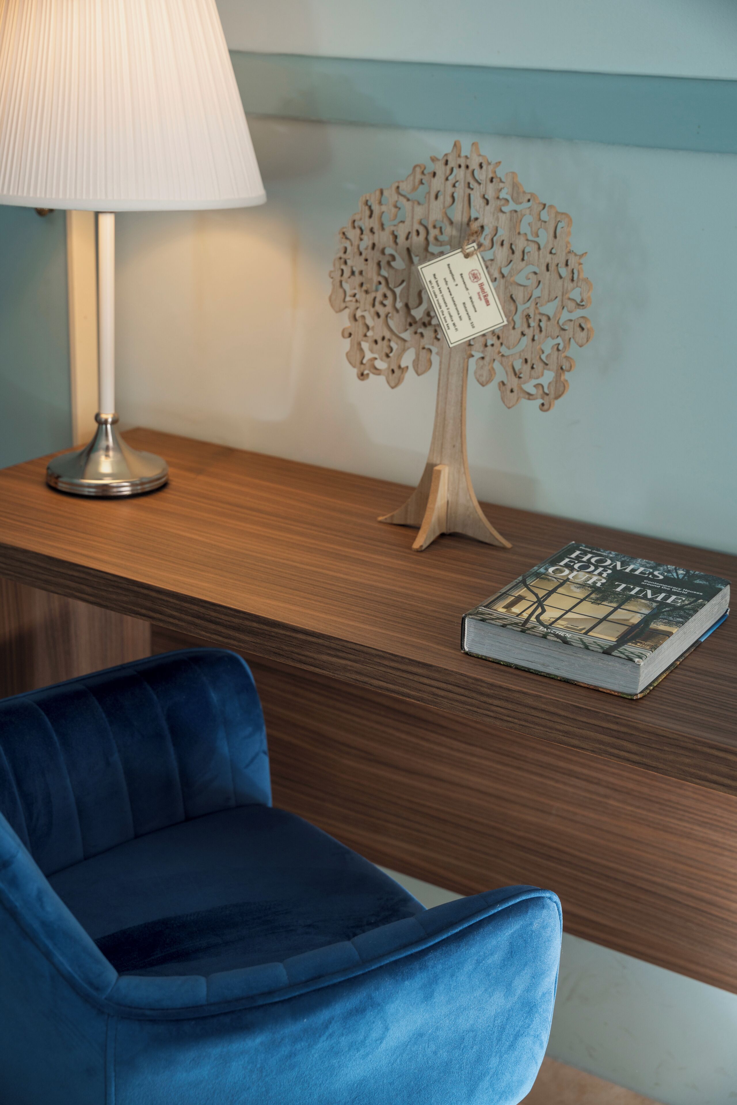 Uma escrivaninha de madeira com uma lâmpada, uma árvore decorativa e um livro intitulado 'Homes for Our Time'.