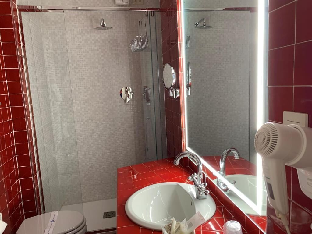 Un baño con pared de baldosas rojas, un lavabo blanco, un espejo y un secador de pelo de mano.