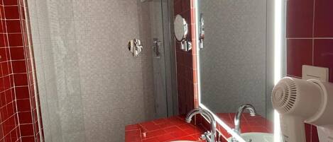 Un baño con pared de baldosas rojas, un lavabo blanco, un espejo y un secador de pelo de mano.