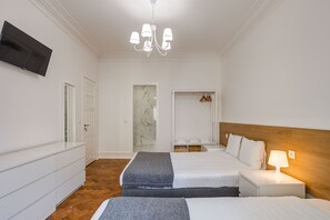 Une chambre d’hôtel avec deux lits, un téléviseur fixé au mur, un lustre, une tête de lit en bois et un mur en marbre.