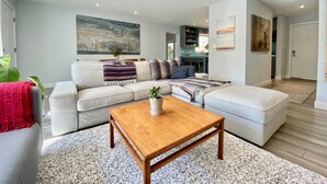 A modern living room with a sectional sofa, a wooden coffee table, and a large abstract painting on the wall. - ‘Garden House’ - Beautiful Mid-Century Home (Tucson)