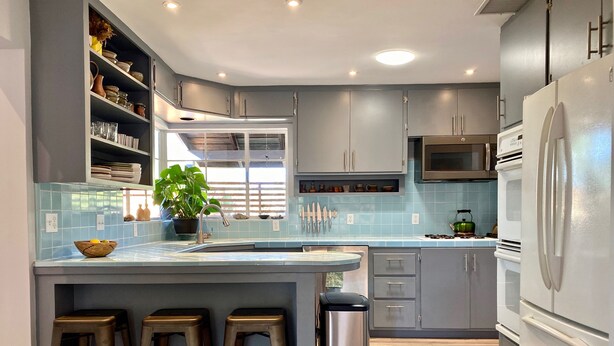 A modern kitchen with grey cabinets, a central island with stools, a stainless steel trash can, and a microwave. - ‘Garden House’ - Beautiful Mid-Century Home (Tucson)