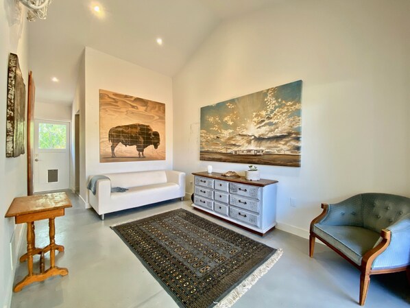 A spacious living room with a white sofa, a grey armchair, a wooden coffee table, a patterned rug, and two large wall-mounted paintings. - ‘Garden House’ - Beautiful Mid-Century Home (Tucson)