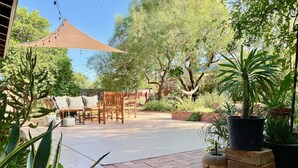 An outdoor patio area with wooden furniture, potted plants, and a shaded area. - ‘Garden House’ - Beautiful Mid-Century Home (Tucson)