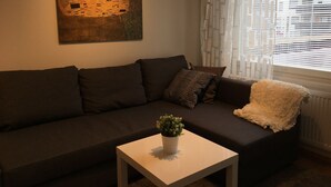 Una sala de estar con un sofá marrón oscuro, una mesa de centro blanca con una planta y un cuadro grande en la pared.