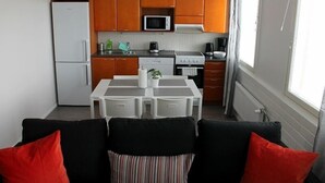 A compact kitchen with wooden cabinets, a refrigerator, microwave, stove, and a dining table with chairs. - Kotimaailma Apts Joensuu Koskikatu 11 (Joensuu)