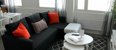 A modern living room with a black sofa, red and striped pillows, a white coffee table, and a patterned rug.