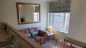 A living room with a sofa, a table with a lamp, a wooden chair, a large mirror, and a window with a view of a brick building. - 71 Micklegate - Apartment 2 (York)