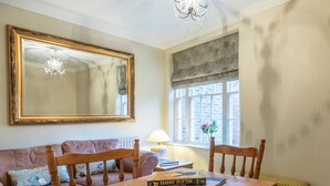 A dining area with a wooden table, chairs, a chandelier, a large mirror, and a window with a view of the outside. - 71 Micklegate - Apartment 2 (York)
