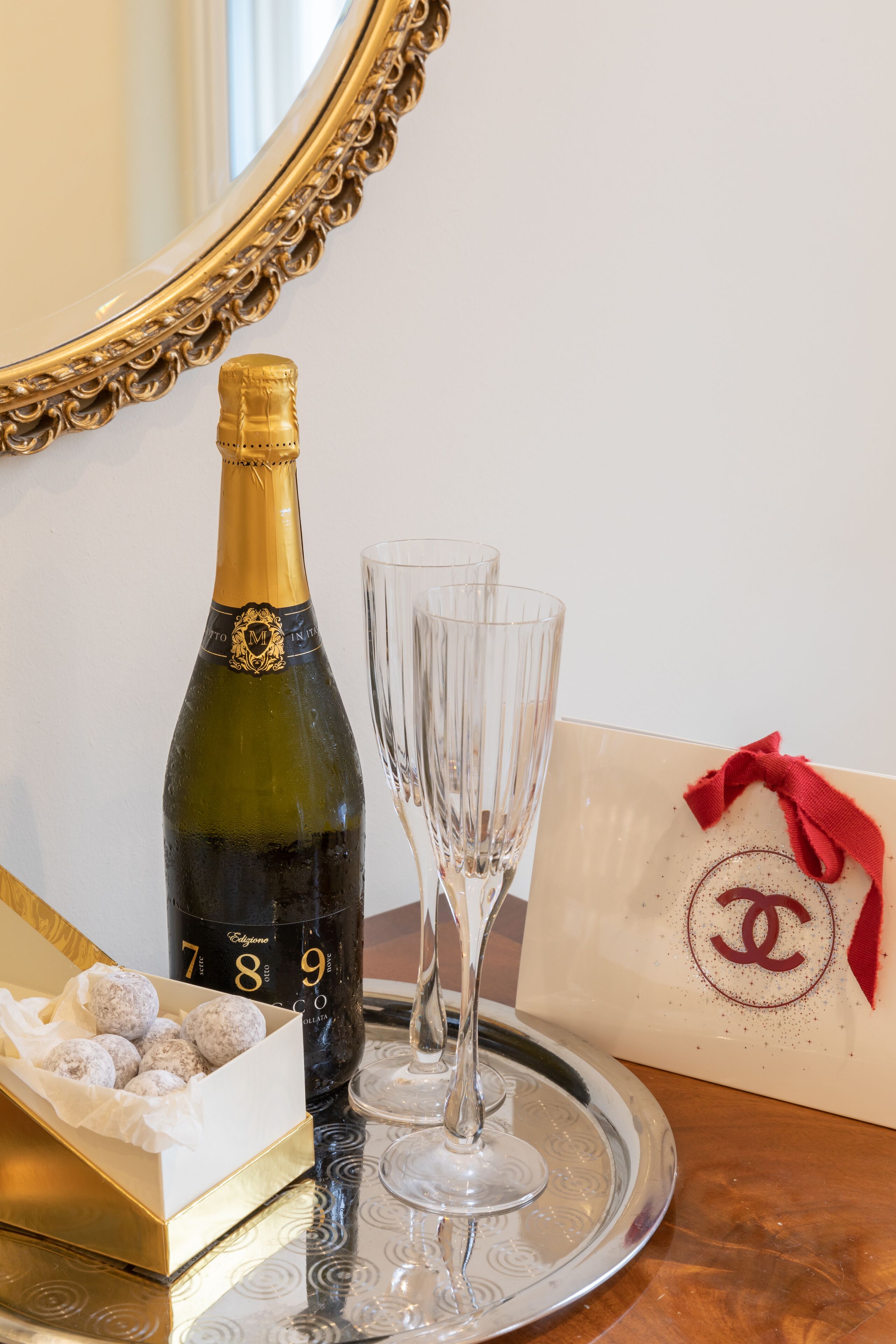 Une bouteille de champagne, deux verres, un plateau, une boîte de chocolats et un sac cadeau avec un ruban rouge.